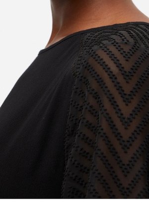 Black top with a sheer patterned sleeve featuring raised zigzag stripes on the shoulder and upper arm against light skin tone.
