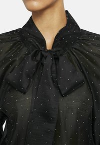 Black sheer blouse with a high neck, bow tie, and scattered silver dot embellishments. Features puffed sleeves and a lightweight texture.