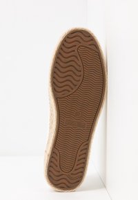 Semelle d'une espadrille beige avec un dessin de bande de roulement ondulée et le logo "Anna Field" sur la semelle en caoutchouc marron.