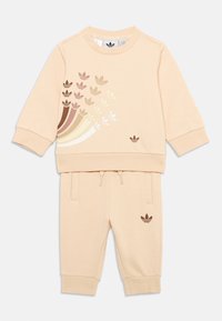 Ensemble de survêtement bicolore beige clair fabriqué en tissu doux. Comprend un sweat-shirt à encolure ras du cou avec des motifs de feuilles multicolores et un pantalon de jogging assorti.