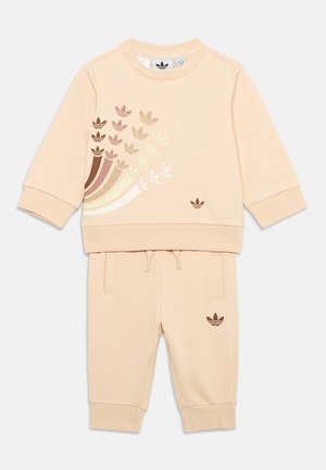 Lys beige to-delt joggedrakt laget av myk stoff. Inkluderer en sweatshirt med rund hals med flerfargede bladmønstre og matchende joggebukser.