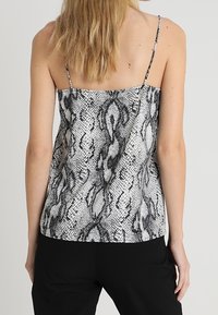 Svart och vit ormskinnsmönstrad linne med tunna band, lös passform och mjuk textur, med en rak nederkant och minimala detaljer i hårdvara.