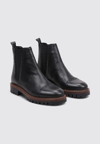 Black leather ankle boots with a textured upper, smooth toe cap, elastic side panels, and a rugged sole. Brown trim around the sole.