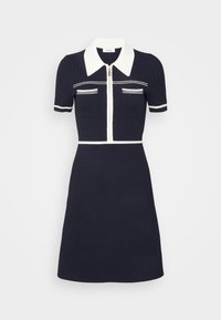 Granatowa sukienka z krótkimi rękawami, białym kołnierzykiem i białym zamkiem. Posiada dwie kieszenie na piersi oraz białe poziome paski wzdłuż dekoltu.