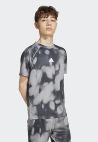 Sivá športová tričko s tie-dye vzorom so svetlými a tmavými škvrnami. Má krátke rukávy a okrúhly výstrih s logom.