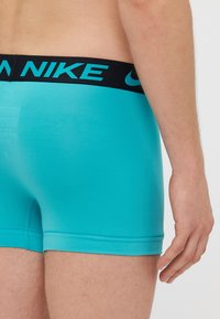 Tirkizne bokserice s crnim pojasom na kojem je u tirkiznoj boji istaknut brend "NIKE". Glatka tkanina s prilagođenim oblikom i kratkim dizajnom nogavica.