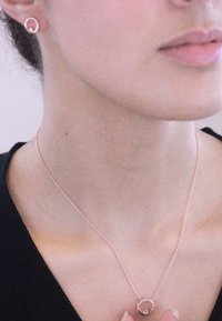 Collana in oro rosa con pendente circolare e piccola pietra; orecchini a bottone circolari abbinati. Catena in metallo liscia con link delicati.