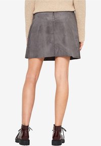 Grijze faux suede rok met een uitlopend ontwerp, tot halverwege de dijen, en een ritsdetail aan de achterkant. Gepaard met glanzende bordeauxrode enkellaarzen.