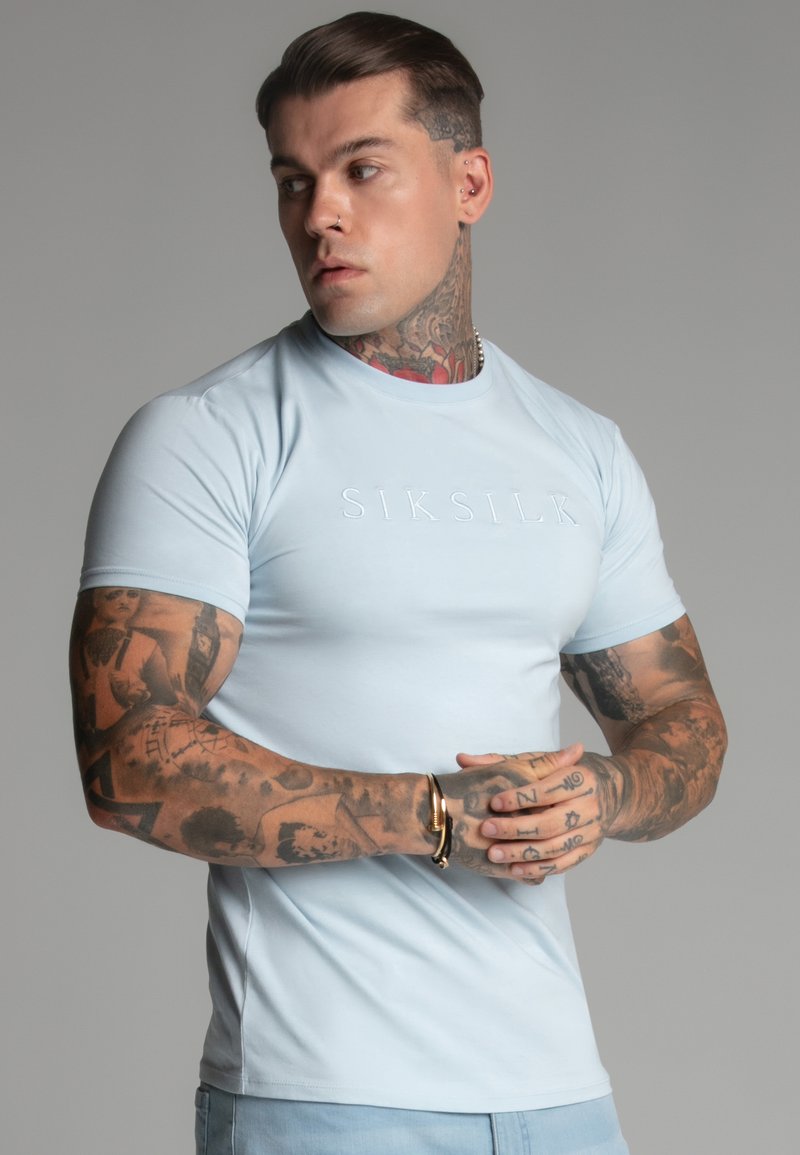 Fénykék, testhezálló póló, sima anyagból, a mellkason feltűntetett "SIKSILK" logóval. Rövid ujjú, kerek dekoltázsú, minimalista dizájn.