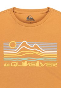 Rostfärgad T-shirt med en grafik av stiliserade sol, berg och vågor i gult, blått och vitt ovanför Quiksilver-logotypen.