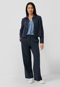 Granatowa krótka kurtka na jasnoniebieskim koronkowym topie, zestawiona z szerokimi granatowymi spodniami i białymi sneakersami. Zastosowano fakturowane tkaniny i guziki.