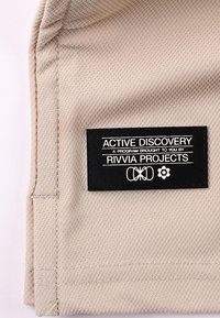 Beiger Stoff mit einer strukturierten Oberfläche trägt ein schwarzes Etikett. Das Etikett zeigt den Schriftzug „ACTIVE DISCOVERY“ sowie Logos und Programmdetails.