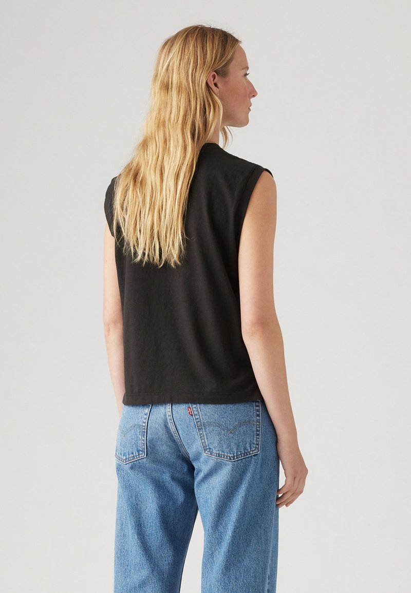Schwarzes ärmelloses Oberteil mit entspannter Passform, aus Baumwolle gefertigt, kombiniert mit hellblauen Jeans aus Denim, die über Gesäßtaschen und ein dezentes Logo-Detail verfügen.