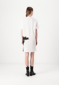 Balta trumpa rankovėmis suknelė su juodu abstrakčiu raštu apatinėje nugaros dalyje. Lygus audinys, tiesus siluetas, iki kelių ilgio, derinama su juodais auliniais batu.