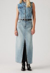 Ljusblå denim ärmlös klänning med knäppning framtill, sprund och svart bälte. Har två bröstfickor och en figursydd silhuett.