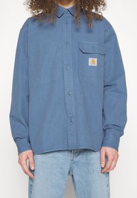 Blauw katoen overhemd met lange mouwen. Voorzien van een knoopsluiting, puntige kraag en een borstzak met een logo-opdruk. Dikke stof.