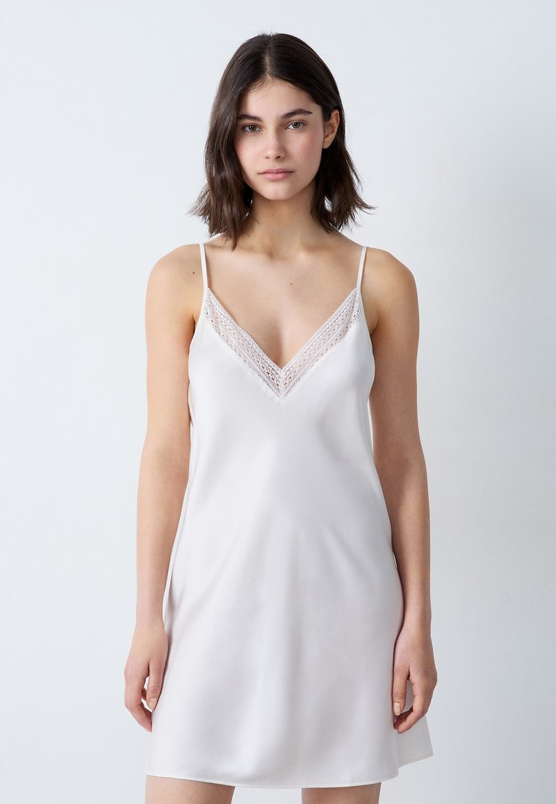 Vestido de seda sin mangas en beige claro con tirantes ajustables, con escote en V y un intrincado encaje a lo largo del escote.