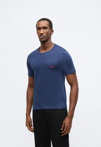 Tamsiai mėlynas medvilninis marškinėlis su apvalia apykakle ir trumpomis rankovėmis. Kairėje krūtinės pusėje yra mažas raudonas „HUGO“ logotipas. Lygi tekstūra.