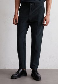 Czarne dopasowane spodnie o kroju slim fit, z delikatnymi szwami z przodu, zapinane na guzik i płaskimi kieszeniami. W połączeniu z czarnymi sznurówkami.