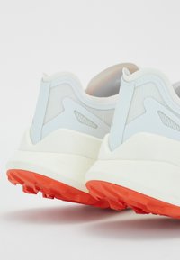 White and light blue running shoes with a textured upper, featuring orange rubber soles and distinct heel design with cutouts.