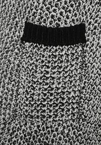 Suéter de punto en tonos negro y gris, con un patrón texturizado y un bolsillo ribeteado negro. Tejido suave y grueso.