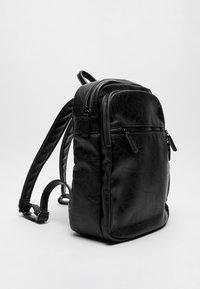 Mochila negra de cuero sintético texturizado. Cuenta con dos bolsillos frontales con cremallera y correas de hombro ajustables. Diseño elegante, forma minimalista.