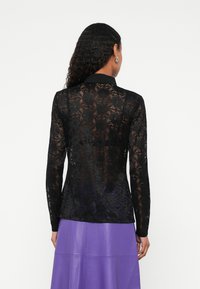 Crni čipkasti top s dugim rukavima i ovratnikom, poluprozirni cvjetni uzorak, uski kroj, upareno s ljubičastom kožnom suknjom.