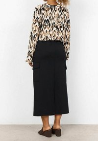 Jupe noire longue avec poches latérales, associée à un haut à manches longues beige et noir à motifs, avec une coupe décontractée et une texture lisse.