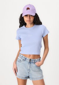 T-shirt a maniche corte a coste di colore azzurro chiaro con scollatura a girocollo, abbinata a pantaloni corti di jeans chiari a vita alta con chiusura a bottone e tasche.