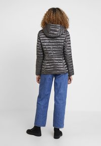 Gepolsterte graue Jacke mit Kapuze, ausgestattet mit horizontalen Nähten, kombiniert mit lockeren blauen Jeans und schwarzen Ankle Boots. Strukturierte, glänzende Oberfläche.