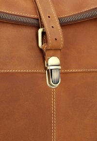 Ruda odinė rankinė su žalvarine sagtimi, turinti užtrauktuką ir kontrastinį siūlą. Paviršius lygus, atskleidžiantis sodrią, šiltą spalvą.