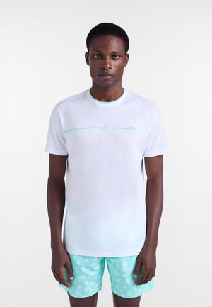 Biały t-shirt z krótkim rękawem z zielonym akcentem i logo na piersi, zestawiony z jasnoniebieskimi szortami z białym wzorem koralowca.