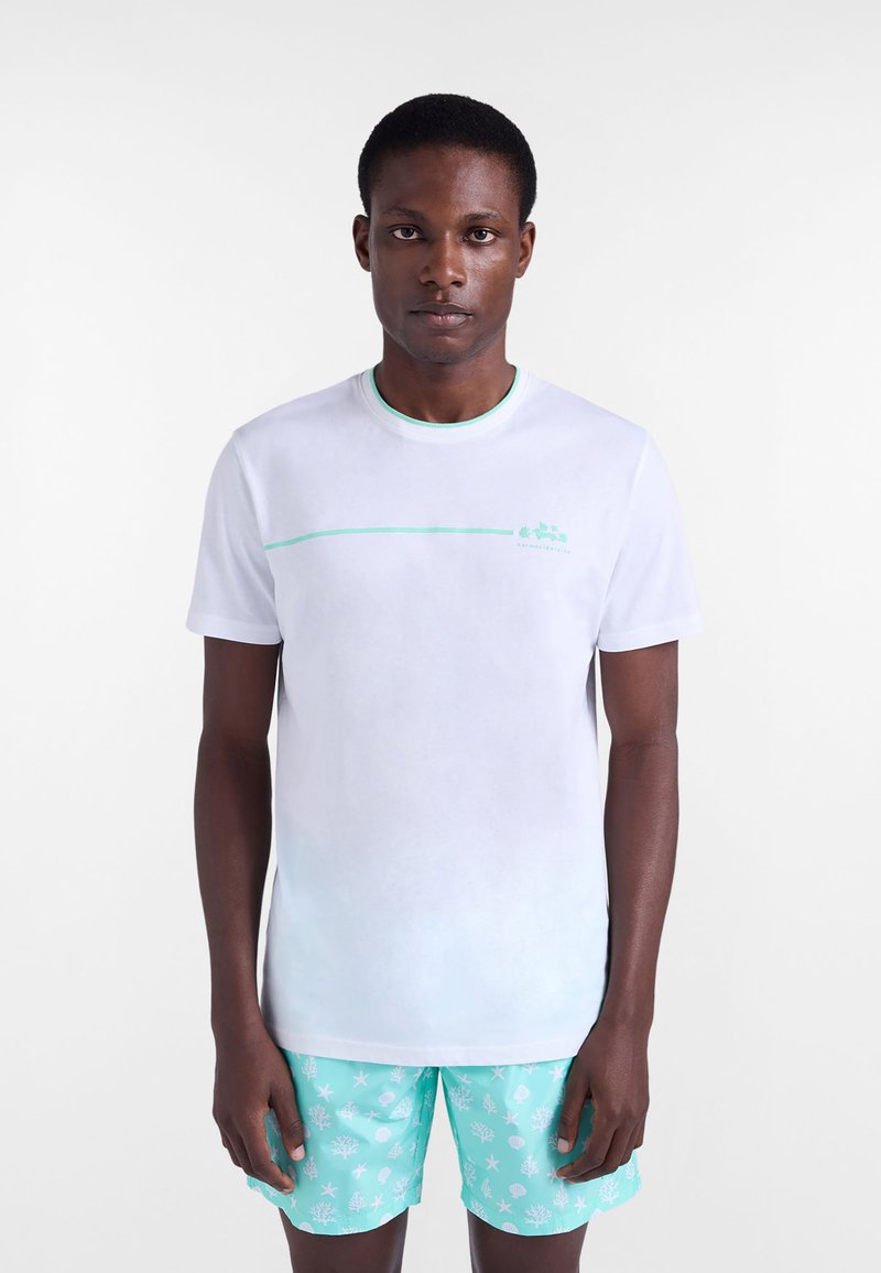 Camiseta blanca de manga corta con una línea de acento verde y logotipo en el pecho, combinada con pantalones cortos azul claro con un patrón de coral blanco.