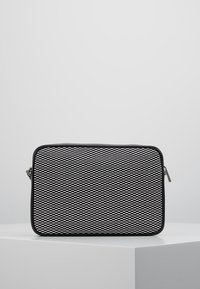 Svartvitt rektangulärt väska med en strukturerad, mönstrad yta och en slät dragkedja. Har rundade hörn och en svart accenttrim.