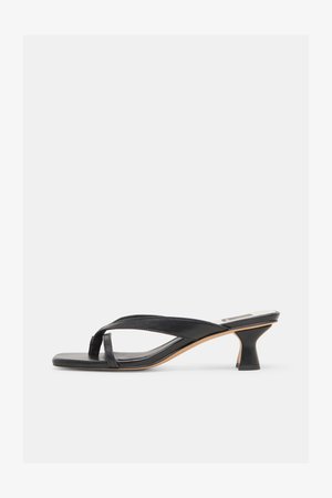 Sandalia de tacón de cuero negro con correa tipo tanga y tacón bajo curvado único sobre fondo neutro.