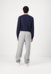 Μπλε ναυτικό φούτερ με μακριά μανίκια σε συνδυασμό με ανοιχτό γκρι φόρμες. Το παντελόνι διαθέτει πίσω τσέπη και άνετη εφαρμογή. Λευκά αθλητικά παπούτσια.