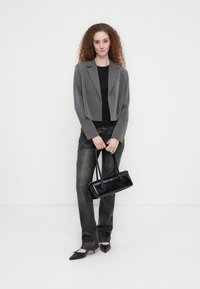 Κομμένο γκρι σακάκι, μαύρο τοπ και γκρι παντελόνι. Μαύρη τσάντα με λεία υφή. Μαύρα μυτερά παπούτσια χωρίς τακούνι. Απλός, ραμμένος σχεδιασμός.