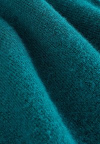 Teal strikket stof med en blød, tekstureret overflade, der har en glat finish og synlige fibre. Materialet er letvægts og let strækbart.