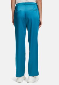 Blå polyester-byxor med vida ben har en slät yta, två bakfickor och är kombinerade med vita sneakers för en komplett look.