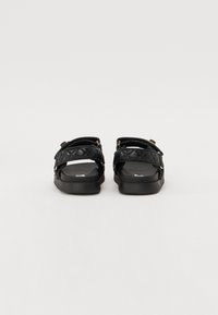 Svarta sandaler med kviltade övre remmar, justerbar hårdvara i guldton, platta sulor och en matt yta. Enkelt design med praktiska funktioner.