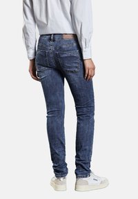 Blå denim skinny jeans med medel tvätt, som har två bakfickor, ljusa sömdetaljer och en märkesetikett vid midjan.