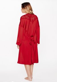 Accappatoio in raso rosso con maniche lunghe, dettaglio in pizzo sul retro e cintura annodata in vita. Tessuto liscio, design alla lunghezza del ginocchio, apertura frontale.