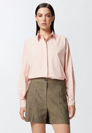 Camicia a maniche lunghe a righe rosa chiaro con colletto, abbinata a pantaloni corti verdi oliva su misura con bottone frontale e pieghe.