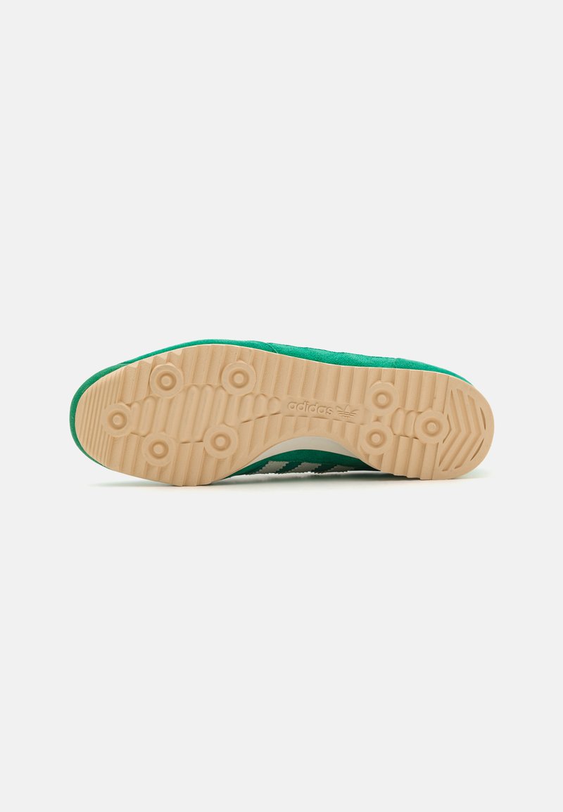 Zielone zamszowe sneakersy z białymi paskami, okrągłym noskiem oraz teksturowaną, tanową gumową podeszwą z okrągłymi wzorami i logotypem po bokach.