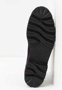 Semelle de chaussure en caoutchouc noir avec des ondulations texturées et des rainures pour une meilleure traction. Présente un marquage à logo, une couleur unie et une construction robuste.