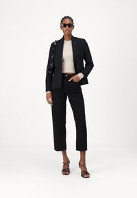 Crni sako s oštrim reverima, priljubljeni kremasti rebrasti top, crne hlače visokog struka i crne sandale s remenčićima. Minimalni dodaci.