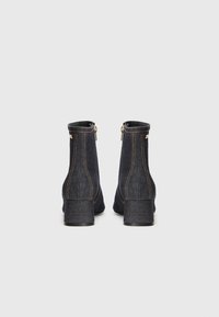 Botas de tornozelo em denim escuro com um alto salto bloco, apresentando detalhes em zíper dourado e costuras em contraste ao longo das costuras.