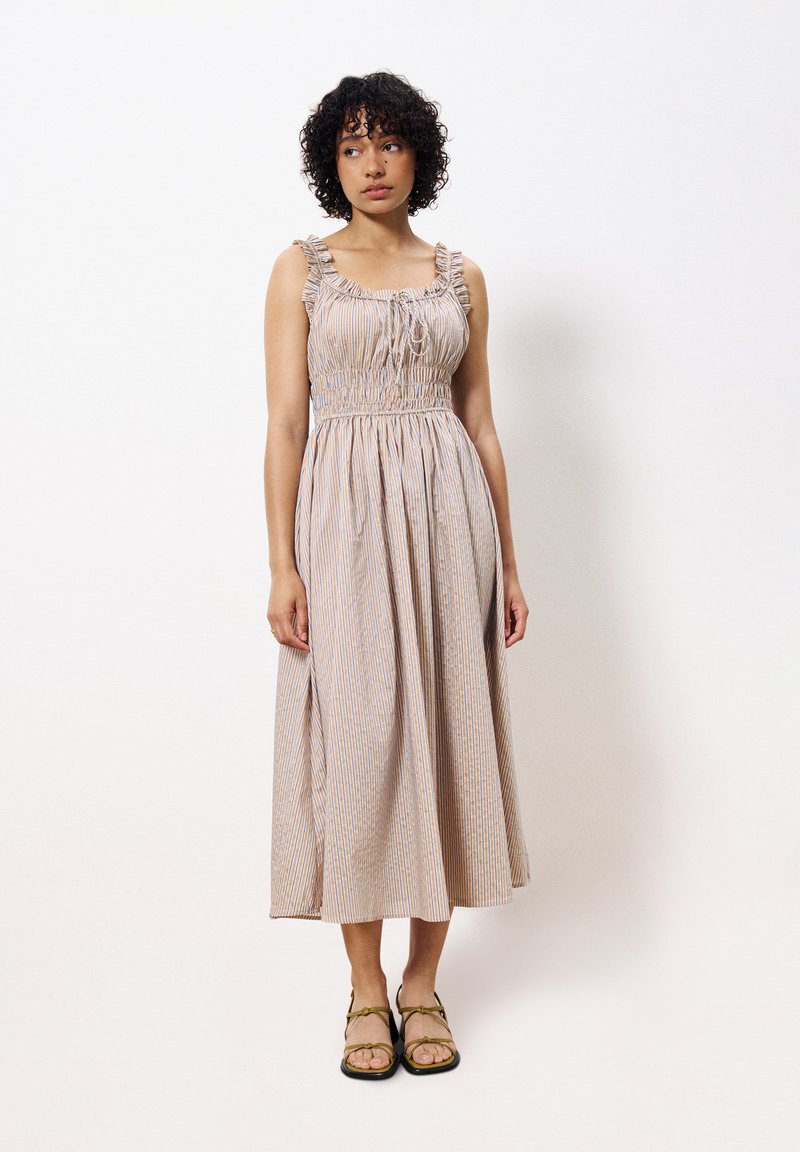 Gestreiftes Maxikleid in Beige mit blauen und orangefarbenen vertikalen Linien. Mit Rüschenträgern, gerafftem Taillenbund und fließendem Rock. Getragen mit Riemchensandalen.