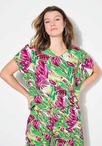 Top a maniche corte, scollo a v, con un motivo tropicale di foglie nei colori verde, rosa e bianco. Tessuto morbido, vestibilità comoda; abbinato a pantaloni coordinati.
