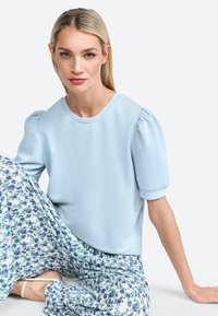 Haut bleu clair à manches courtes avec des épaules bouffantes, associé à un pantalon à motif floral aux tons bleus et verts. Texture lisse.